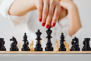 Schwarze Schachfiguren und weibliche Hand mit rotlackierten Fingernägeln