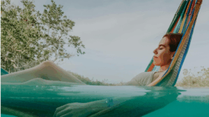 Frau in einer Hängematte, die zur Hälfte im Wasser schwimmt