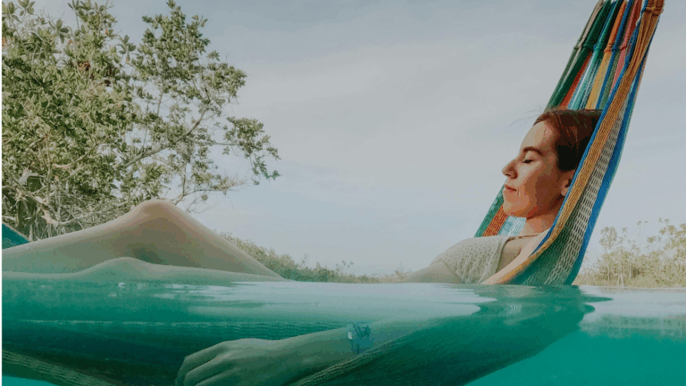 Frau in einer Hängematte, die zur Hälfte im Wasser schwimmt