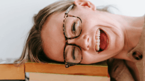 Frau mit Hornbrille legt lachend ihren Kopf auf einen Bücherstapel: Sinnbild für Festgald oder Tagesgeld