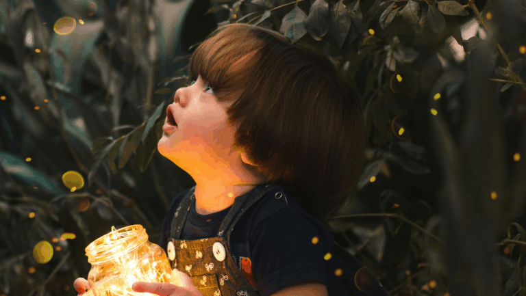 Ein kleiner Junge ist im Profil zusehen, er hält ein Glas mit elektrischen Lichtern in der Hand und schaut nach oben.
