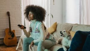 Eine junge Frau sitzt mit ihrem Hund vor dem Fernseher und hält eine Fernbedienung in der Hand