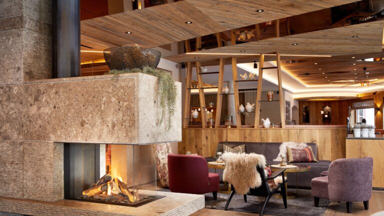 Aufnahme vom Alpin- und Spa-Hotel Tuxerhofi m Zillertal in Tirol: Im Vordergrund sieht man einen Kamin, im Hintergrund einen gemütlichen tisch mit Stühlen