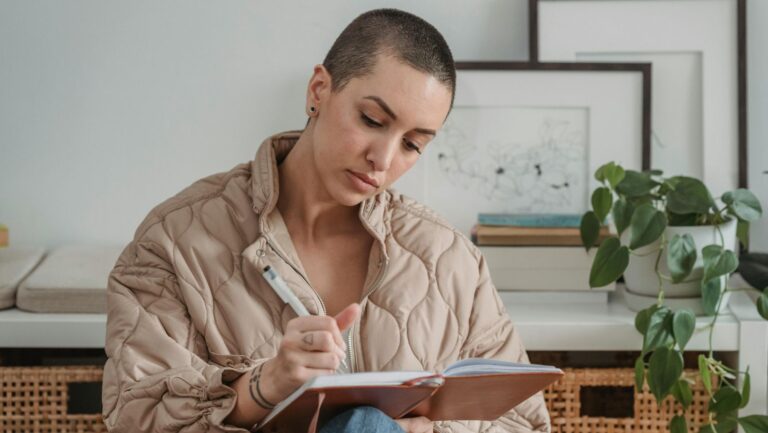 Eine junge Frau mit einem Buzz Cut schreibt in einen Finanzplaner.