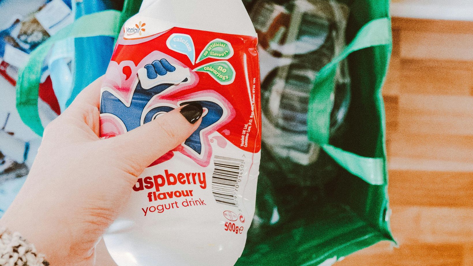 Eine Hand mit schwarz lackiertem Daumennagel hält eine PET-Flasche fest