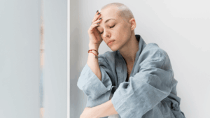 Junge Frau mit raspelkurzen blinden Haaren stützt die Stirn auf die Hand und hält die Augen geschlossen.