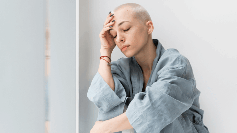 Junge Frau mit raspelkurzen blinden Haaren stützt die Stirn auf die Hand und hält die Augen geschlossen.