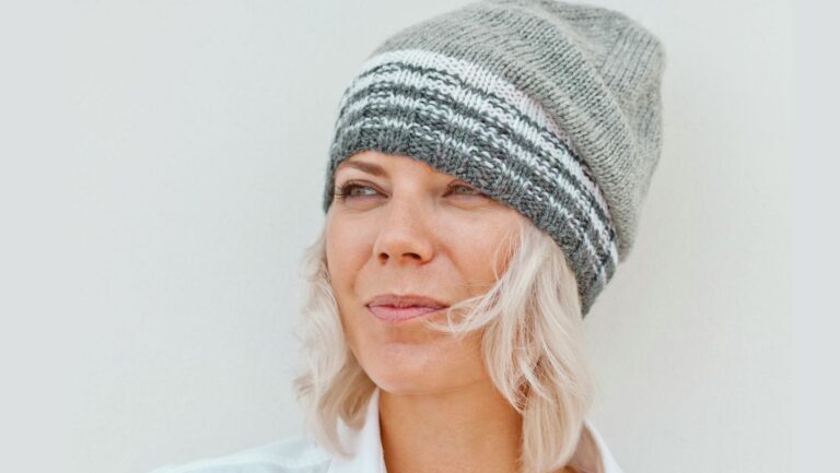 Frau mit weißen halblangen Haaren um die 50 Jahre alt sieht zur Seite. Auf dem Kopf trägt sie eine grau-weiß gestreifte Strickmütze.