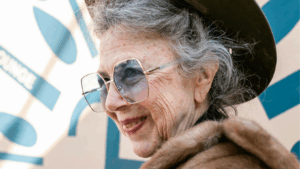 Ältere Frau um die 70, die eine blaugetönte Sonnenbrille trägt und leicht lächelt