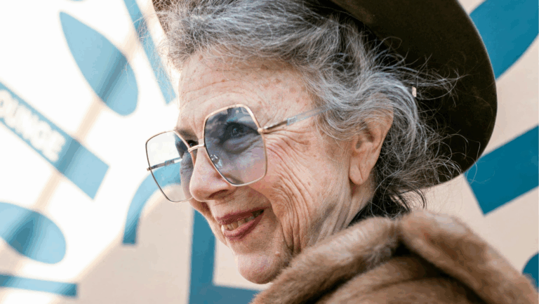 Ältere Frau um die 70, die eine blaugetönte Sonnenbrille trägt und leicht lächelt