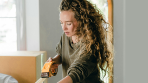 Frau hat einen Paketbandabroller in der Hand und klebt ein Paket zu.