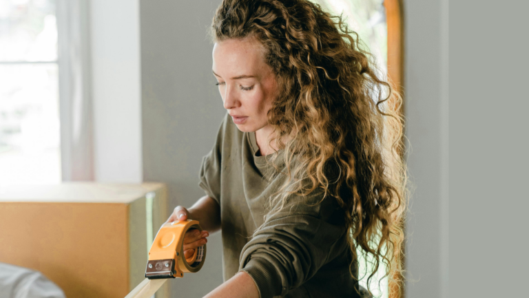 Frau hat einen Paketbandabroller in der Hand und klebt ein Paket zu.