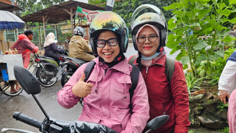 Zwei indonesische Frauen mit Helm und Brille, die offenbar auf einem Motorroller sitzen