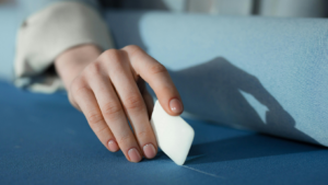 Eine Frauenhand zeichnet mit einem Stück Stoffmalkreide eine Linie auf blauen Stoff