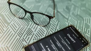 Als Symbolbild für Agentic Finance wird hier ein Smartphone mit Chat GPT gezeigt, daneben eine Brille.