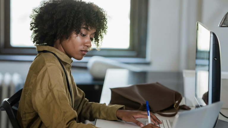 Weibliche Person of Colour sitzt vor dem Laptop und macht sich Notizen