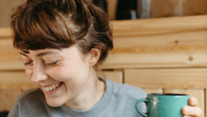 Junge Frau it hochgesteckten haaren und Pony schaut lächelnd nach unten, in der Hand eine grüne Kaffeetasse