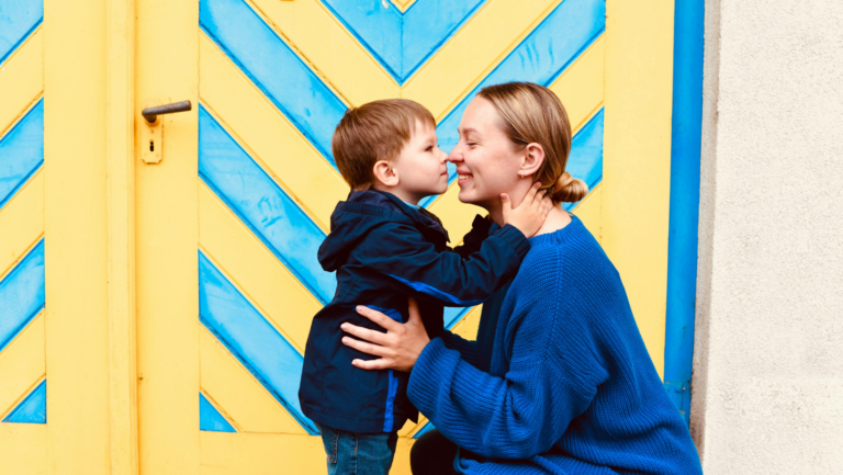 Eine Mutter umarmt ihren kleinen Jungen, die beiden stehen vor einer blau-gelben Tür