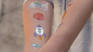 Die Innenseite eines Ars mit Tattoos: eines mit Schrift "Space", eines mit einer Rakete, eins mit einem roten Planeten