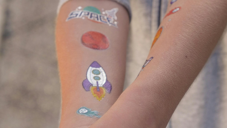 Die Innenseite eines Ars mit Tattoos: eines mit Schrift "Space", eines mit einer Rakete, eins mit einem roten Planeten