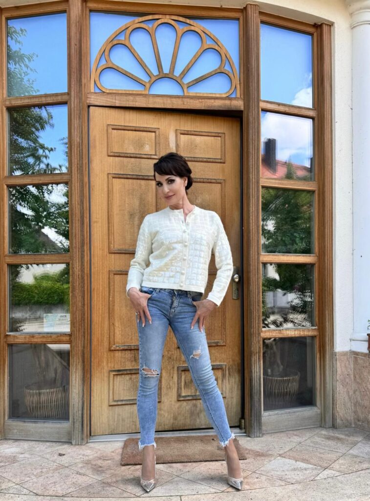 Anna Maria Kaufmann steht in Bluse und Jeans vor einer Haustür in Eiche und guckt selbstbewusst in die Kamera