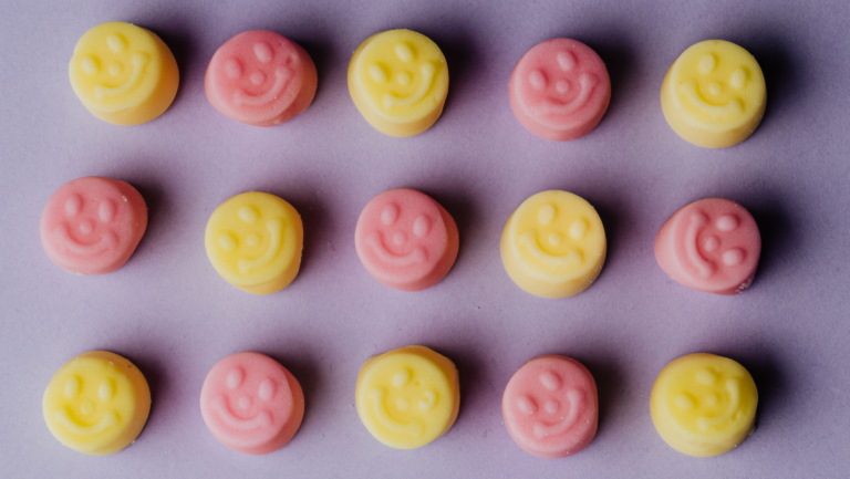 Auf einem violetten Hintergrund liegen abwechselnd pinke und gelbe runde Smileys.