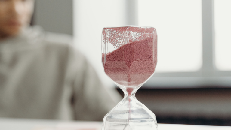 Sanduhr mit Sand in Altrosa, der gerade herunterläuft