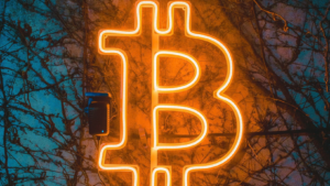 Das B von der Währung Bitcoin als Leuchtbuchstabe auf einer Hauswand mit Ranken