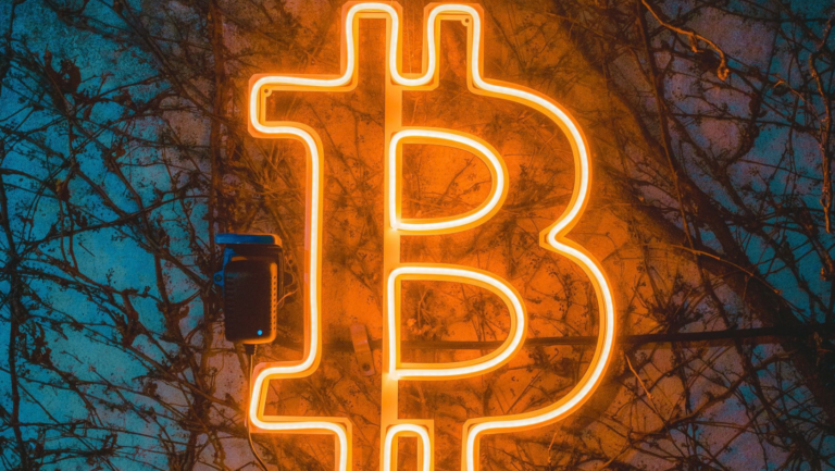 Das B von der Währung Bitcoin als Leuchtbuchstabe auf einer Hauswand mit Ranken