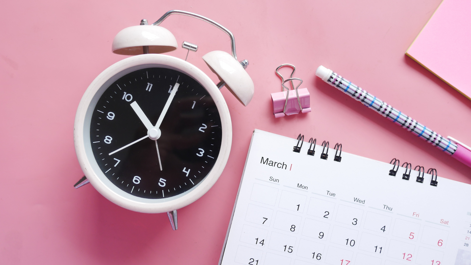 Ein alter manueller Wecker mit Kalender auf rosa Hintergrund