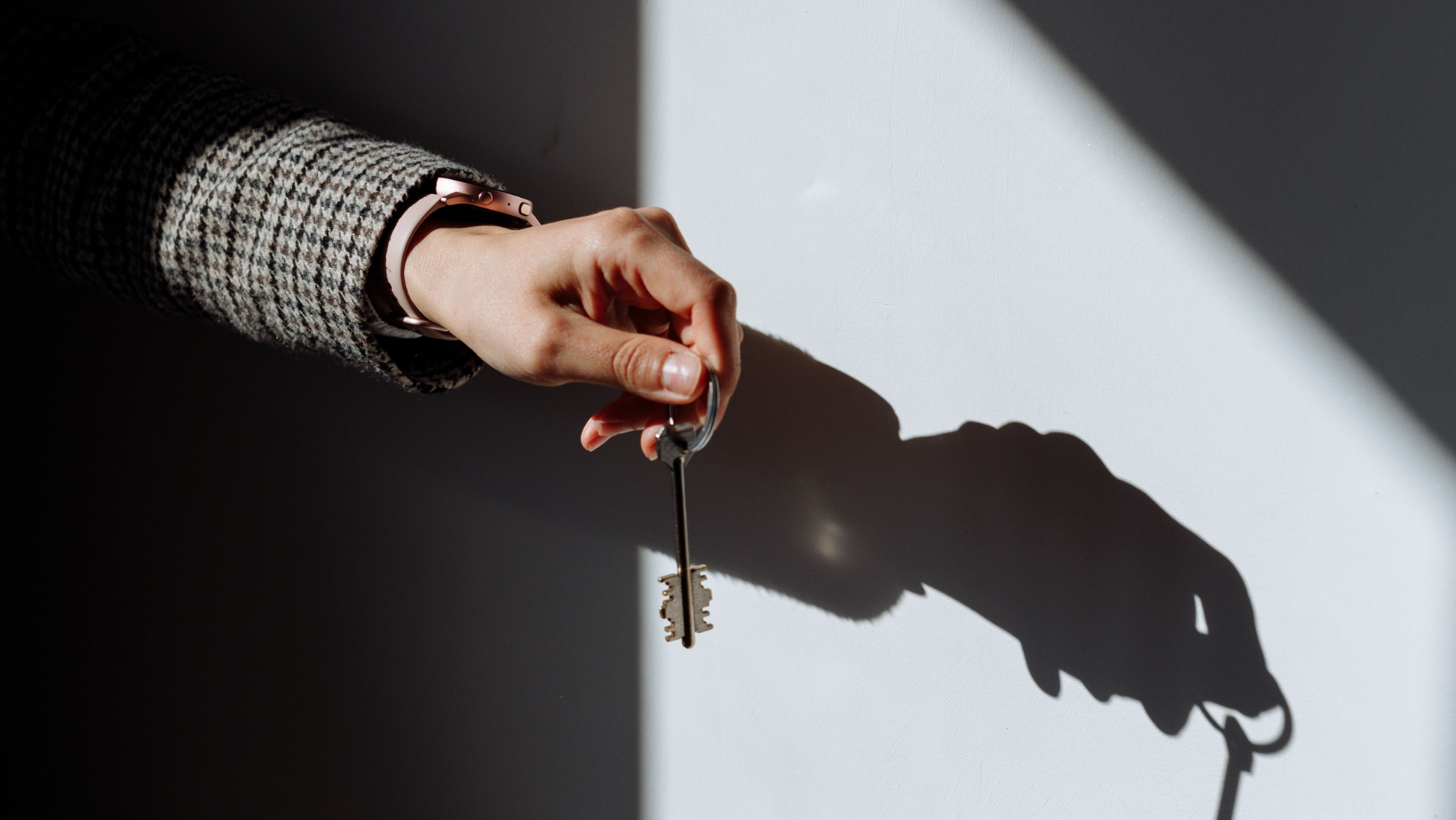 Eine Hand hält einen Schlüssel. Da sie von vorn Licht bekommt, wirft sie einen Schatten.
